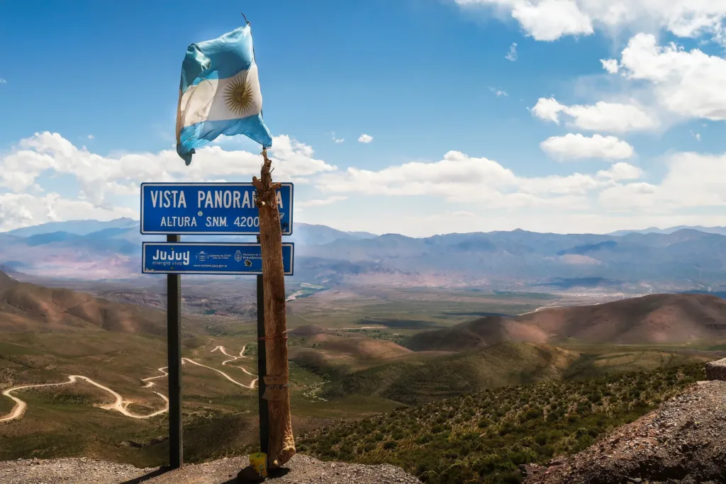 Argentinská vlajka a cedule Vista Panorámica ve výšce 4200 metrů nad horskou krajinou provincie Jujuy.