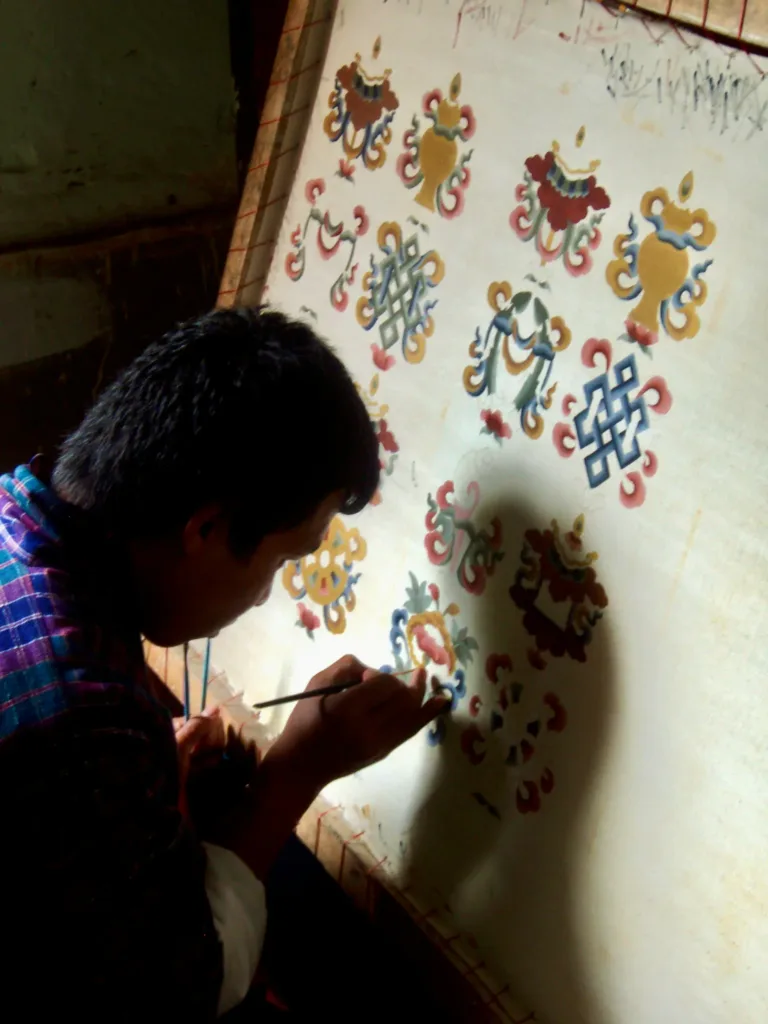 Muž ručně maluje barevné buddhistické ornamenty na světlou textilii.