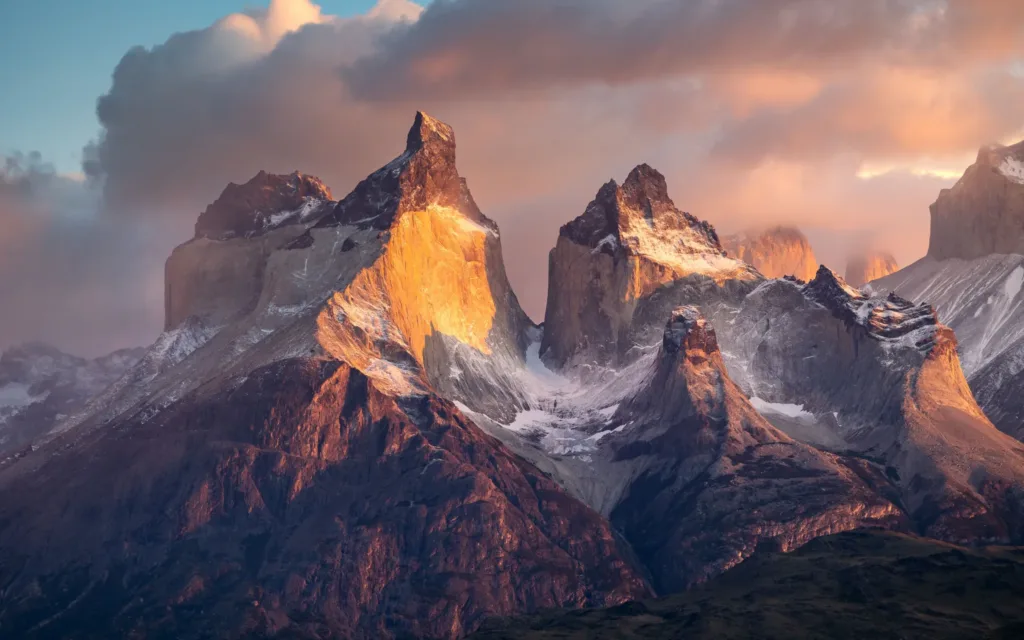 Osvětlené žulové štíty Torres del Paine se zbytky sněhu pod dramatickými mraky.