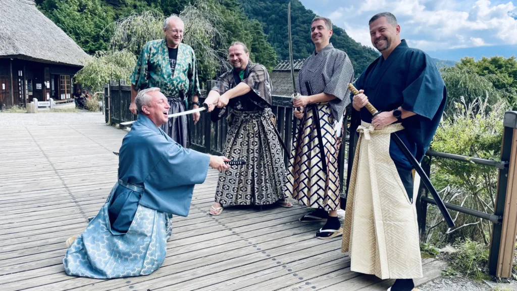 Pět mužů v tradičních japonských oděvech na dřevěné lávce u historické stavby v zeleni