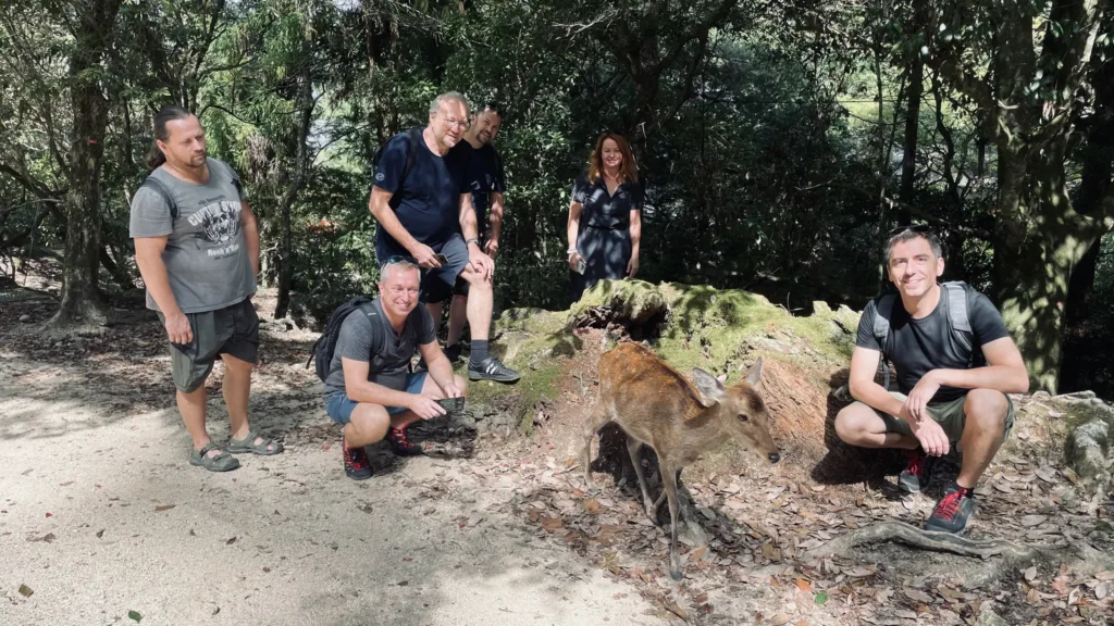 Skupina turistů stojí a dřepí na lesní cestě poblíž divočáka u padlého kmene.