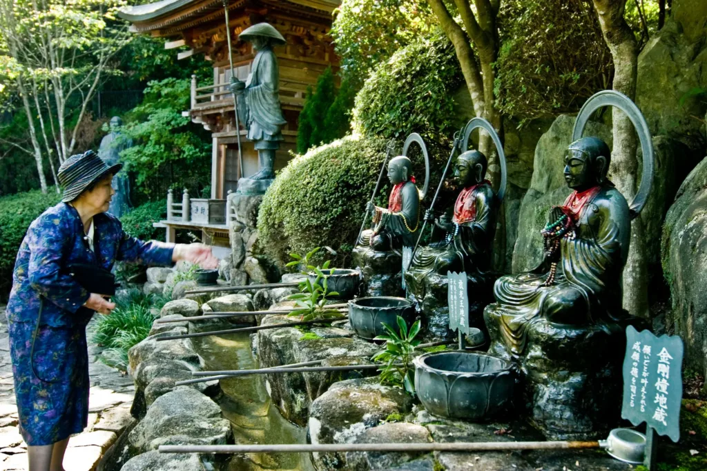 Žena v tradičním oděvu u řady buddhistických soch v zahradě chrámu