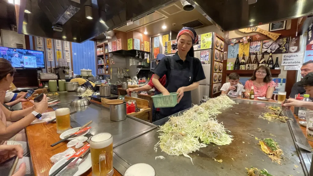 Kuchařka připravuje pokrm na rozpálené plotně před hosty v rušné japonské restauraci.