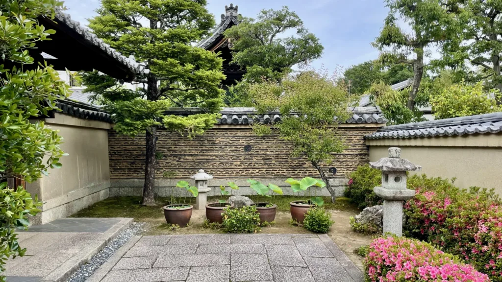 Klidná japonská zahrada s kamennou lucernou, bonsají, květinami a zdí s taškovou střechou