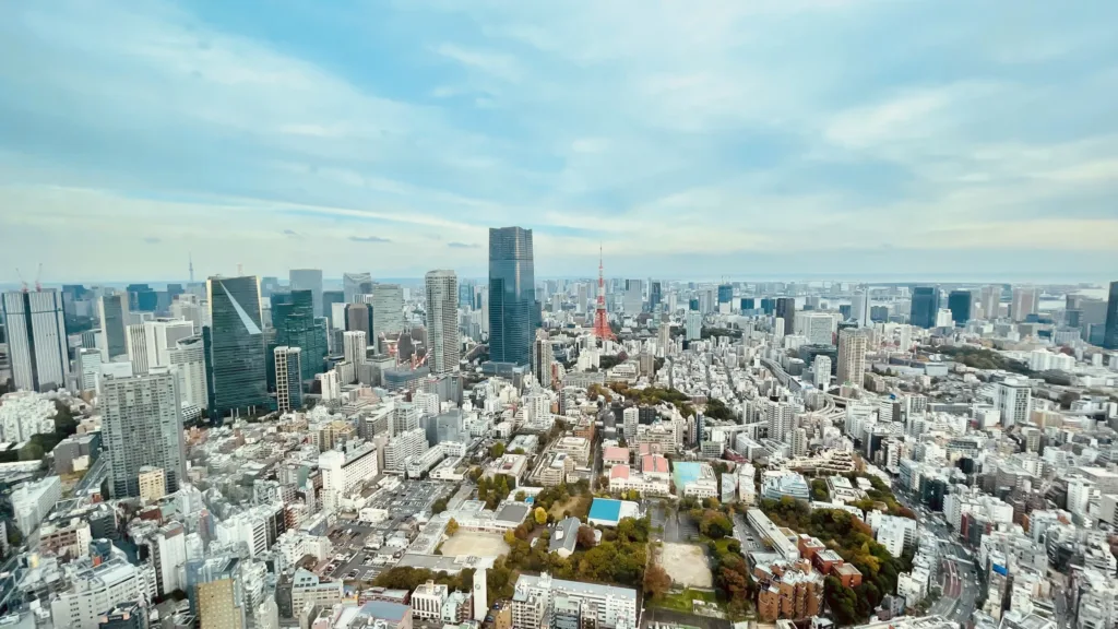 Pohled z výšky na hustou zástavbu Tokia s červenobílou věží Tokyo Tower uprostřed města.