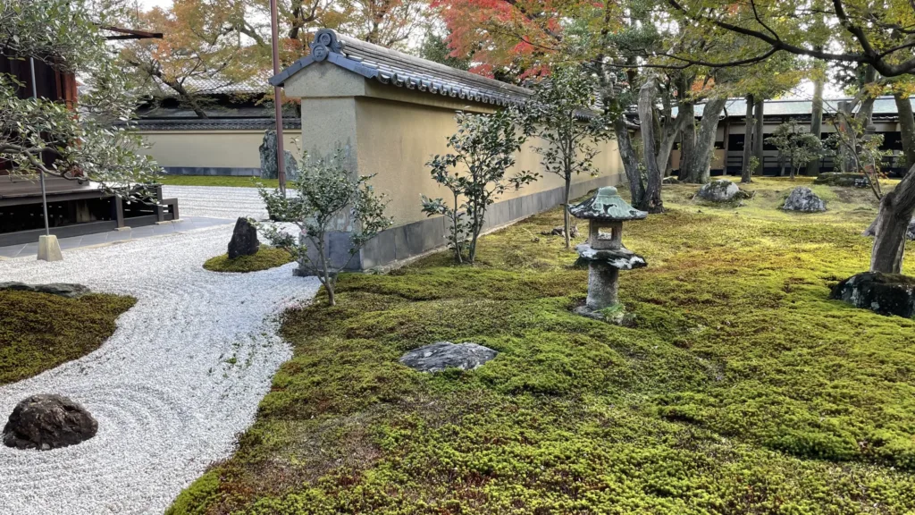 Mechem porostlá japonská zahrada se štěrkovou cestou, kamennou lucernou a podzimně zbarvenými stromy.