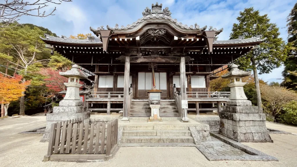 Dřevěná budova tradičního japonského chrámu se schodištěm, kamennými lucernami a podzimním listím.