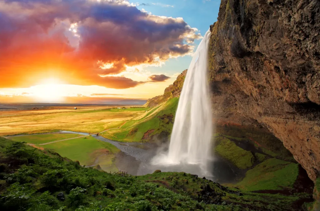 Vodopád Seljalandsfoss padající z útesu do zeleného údolí při západu slunce na Islandu.
