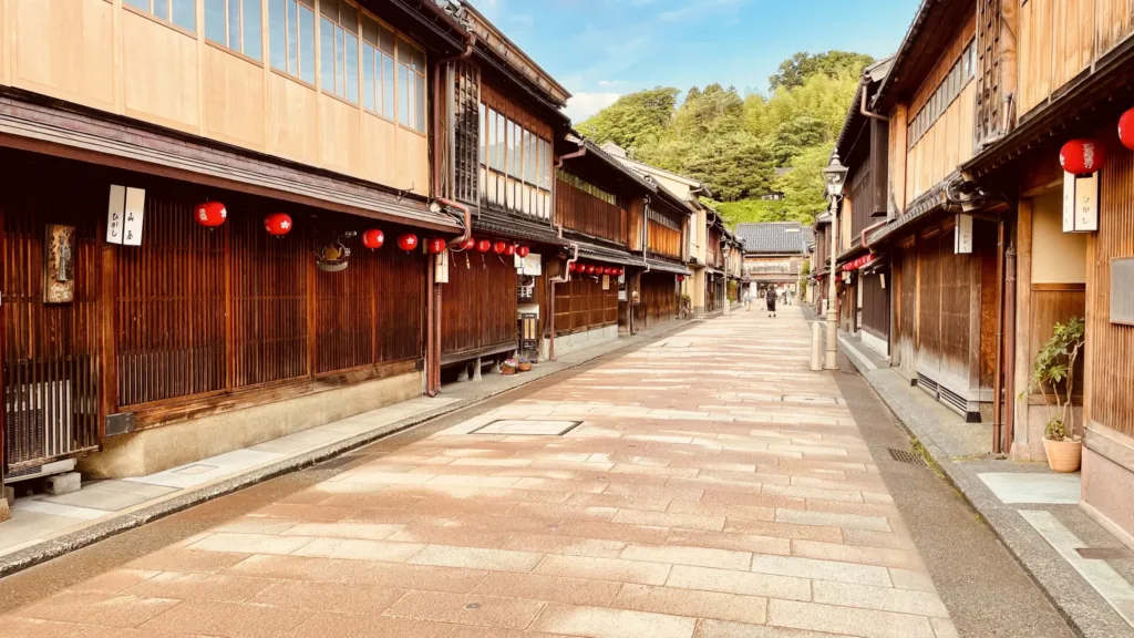 Klidná dlážděná ulice lemovaná tradičními dřevěnými japonskými domy a červenými lucernami.