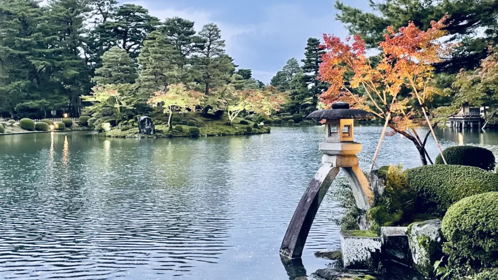 Kamenná lucerna u jezírka v japonské zahradě s červenými podzimními javory