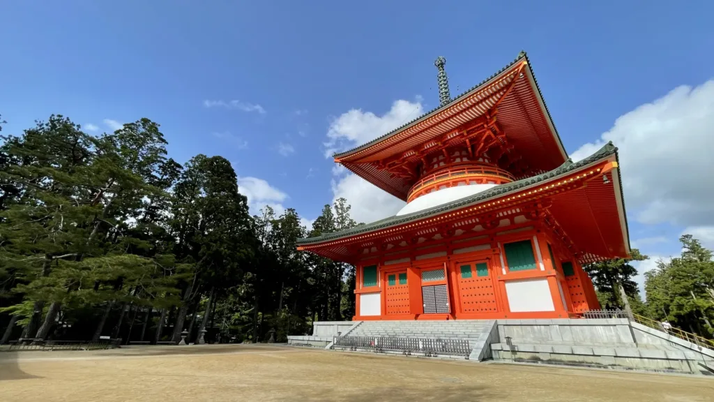 Červenooranžová dvoupatrová brána japonské šintoistické svatyně před stromy a modrou oblohou.