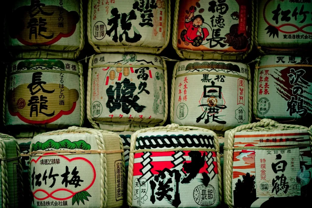Stoh ozdobných slaměných sudů se saké s japonskými nápisy a barevnými motivy.