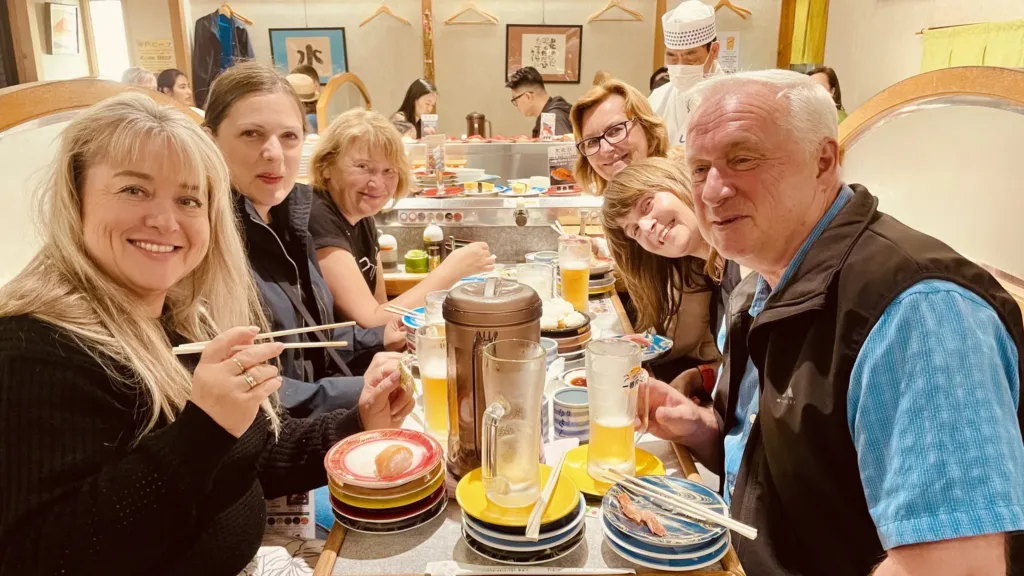 Skupina cestovatelů sedí u stolu v japonské restauraci a jí sushi hůlkami.
