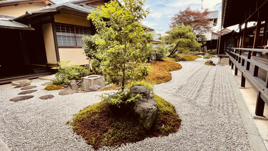 Štěrková zahrada s mechem, kameny a keři mezi tradičními dřevěnými japonskými budovami.