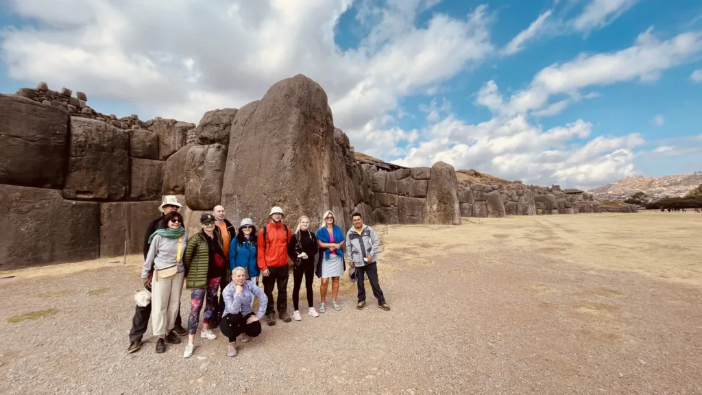Skupina turistů pózuje před mohutnými kamennými zdmi inckého komplexu Sacsayhuamán u Cusca.