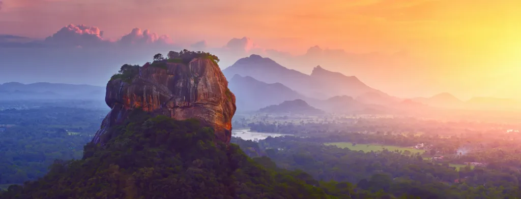 Mohutná skalní pevnost Sigiriya vystupující nad zelenou krajinou Srí Lanky při východu slunce.