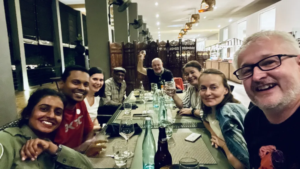 Skupina cestovatelů sedí u dlouhého stolu v restauraci a usmívá se do fotoaparátu.