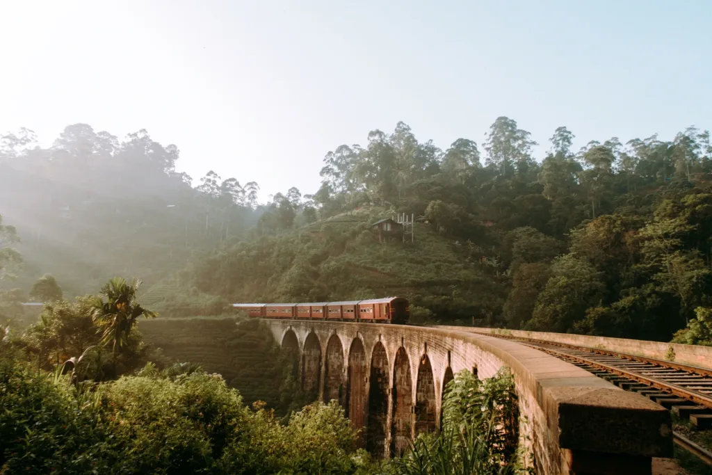 Vlak projíždějící po kamenném mostě Nine Arches Bridge uprostřed zeleného horského lesa