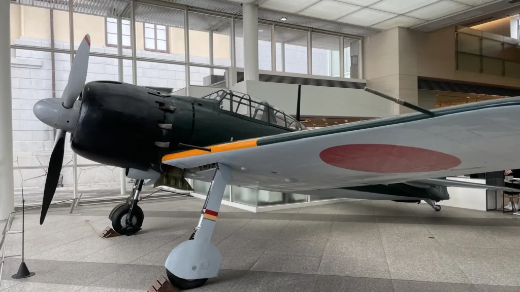 Japonský stíhací letoun Mitsubishi A6M Zero vystavený v prosklené muzejní hale.