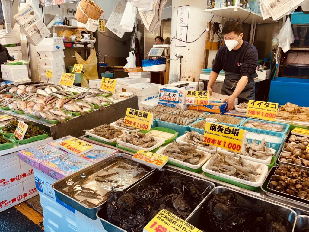 Prodejce v roušce u stánku s čerstvými rybami, krevetami a mušlemi na japonském trhu