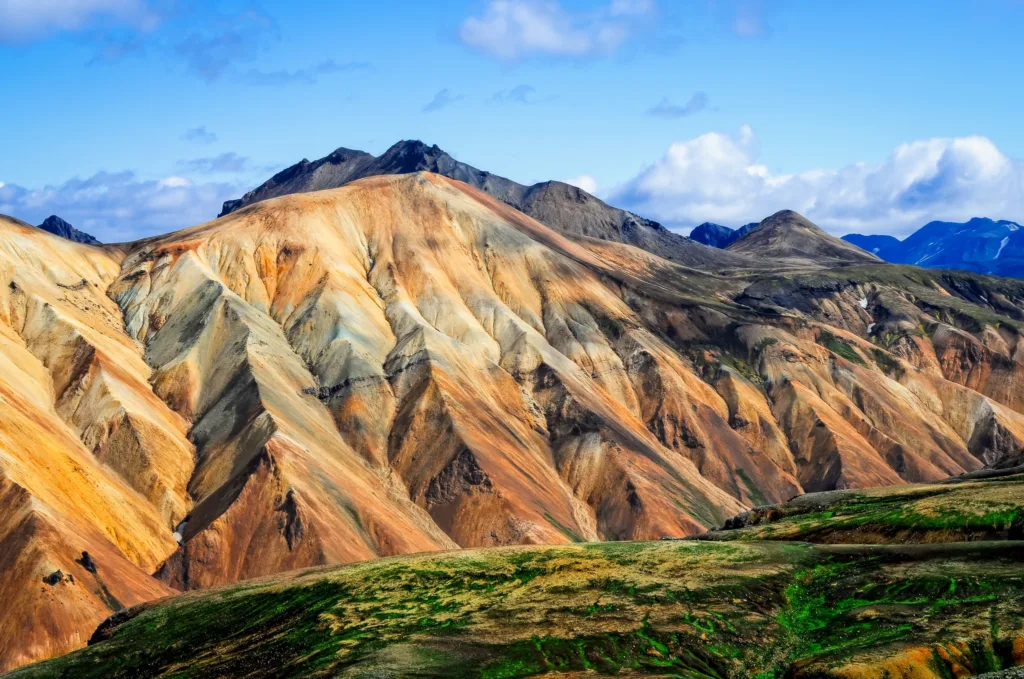 Pestrobarevné sopečné svahy a zelené pláně v horské oblasti Landmannalaugar na Islandu.