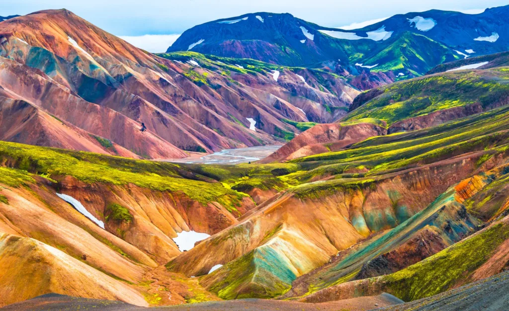 Pestrobarevné sopečné svahy a zelené horské údolí se zbytky sněhu v oblasti Landmannalaugar na Islandu.