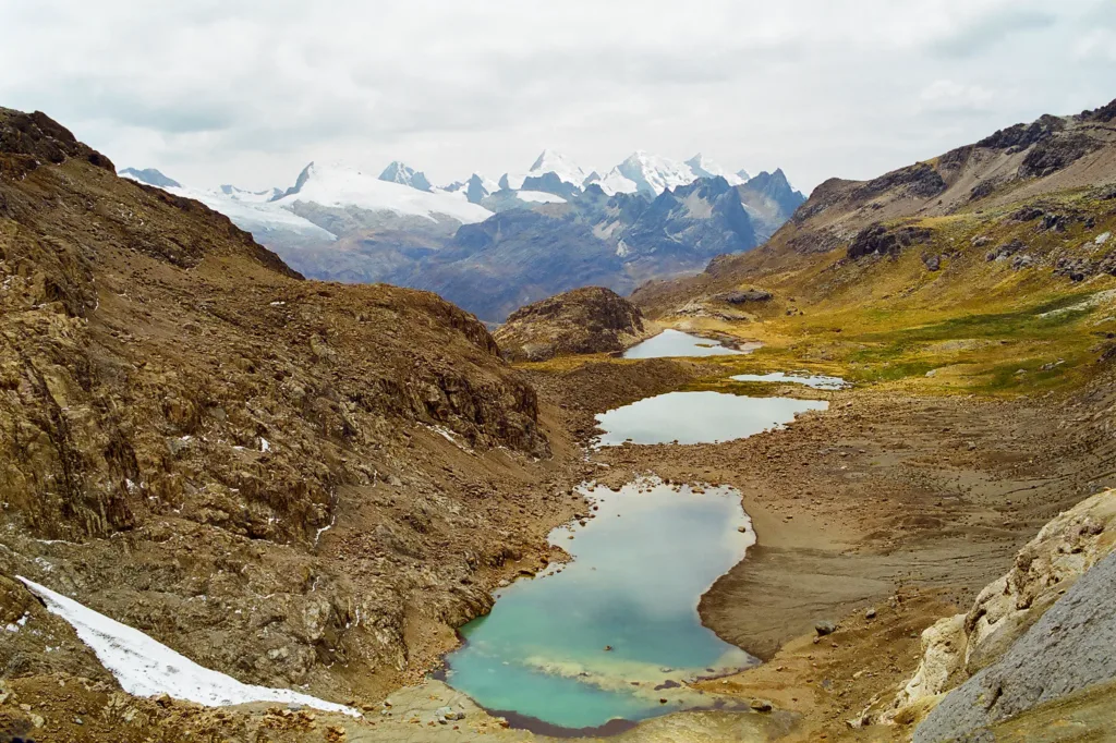 Tyrkysové horské jezírko mezi skalnatými svahy, v pozadí zasněžené alpské štíty.