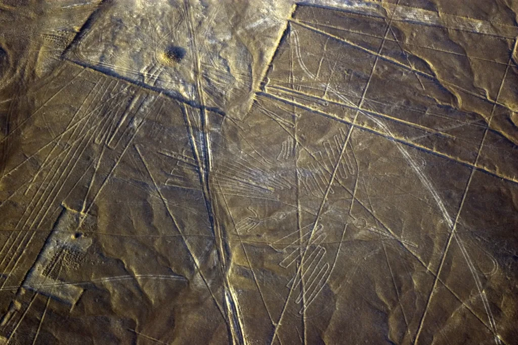 Letecký pohled na světlé ryté linie a geometrické obrazce v tmavé pouštní krajině.