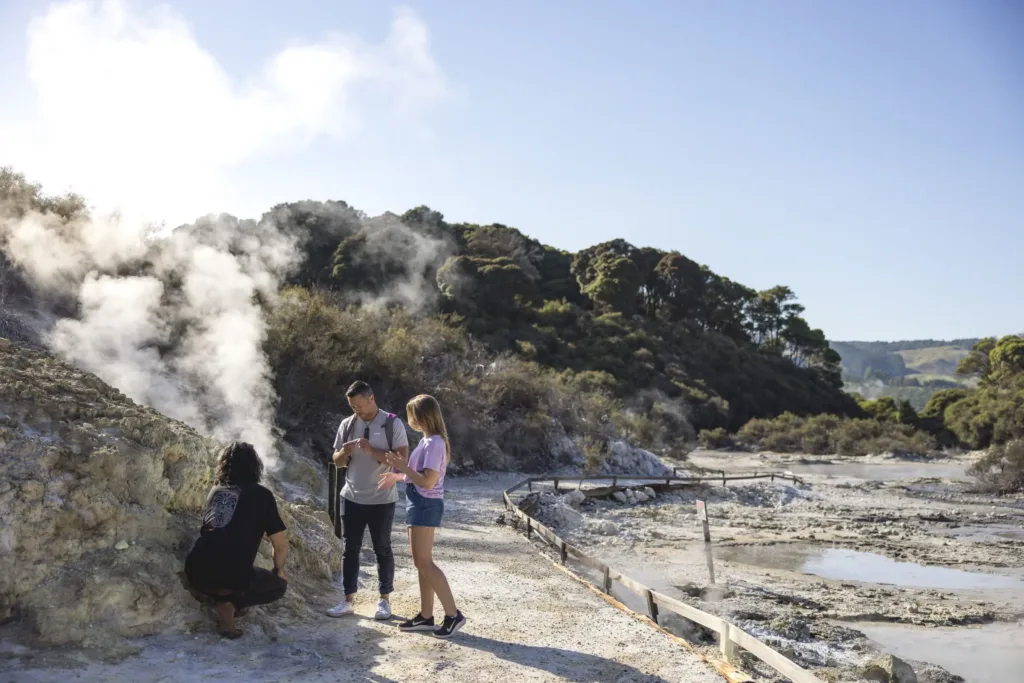 Turisté si prohlížejí kouřící geotermální prameny a bahenní jezírka ve skalnatém údolí