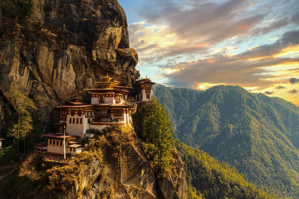 Klášter Paro Taktsang neboli Tygří hnízdo na skalním útesu nad zalesněným horským údolím při západu slunce.