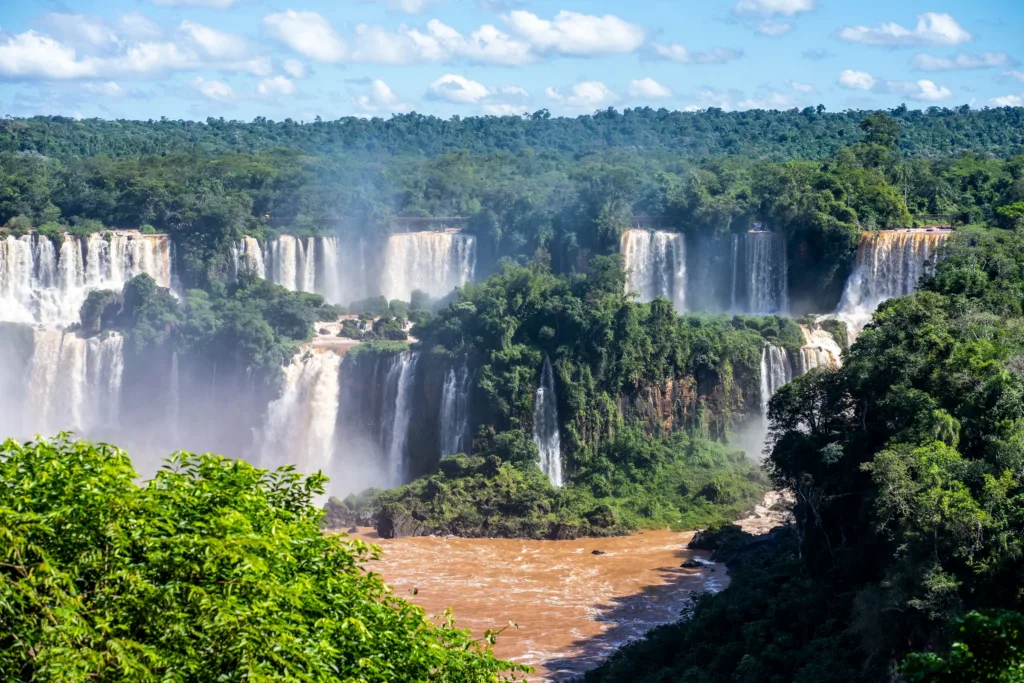 Pohled na několik mohutných vodopádů Iguazú obklopených hustým zeleným pralesem.