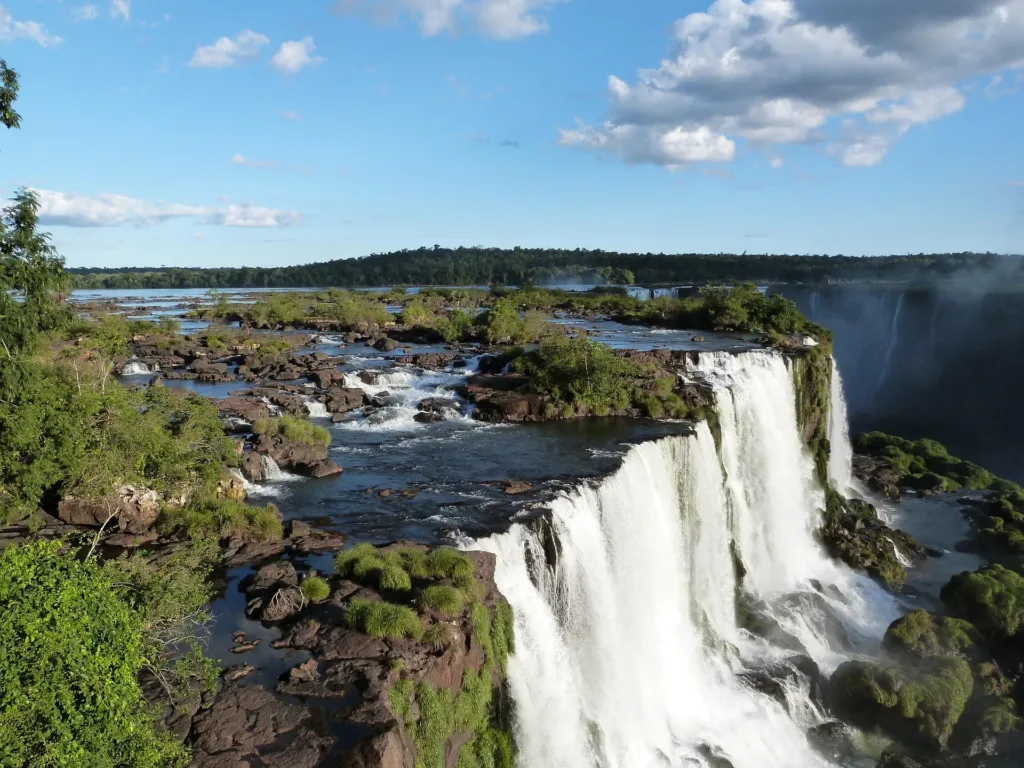 Mohutné vodopády Iguazú padající přes skalnaté terasy mezi zelenou tropickou vegetací.