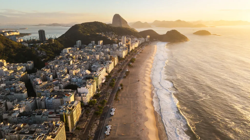 Letecký pohled na pláž Copacabana, hustou zástavbu Ria de Janeira a horu Cukrová homole v pozadí.