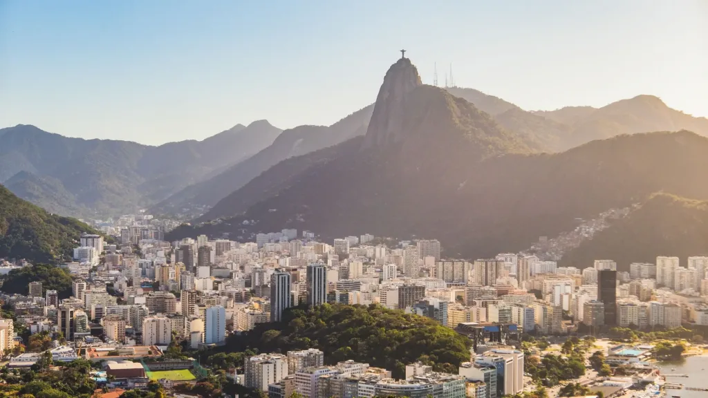 Panoramatický pohled na zástavbu Rio de Janeira pod zelenými horami, s horou Corcovado v pozadí.