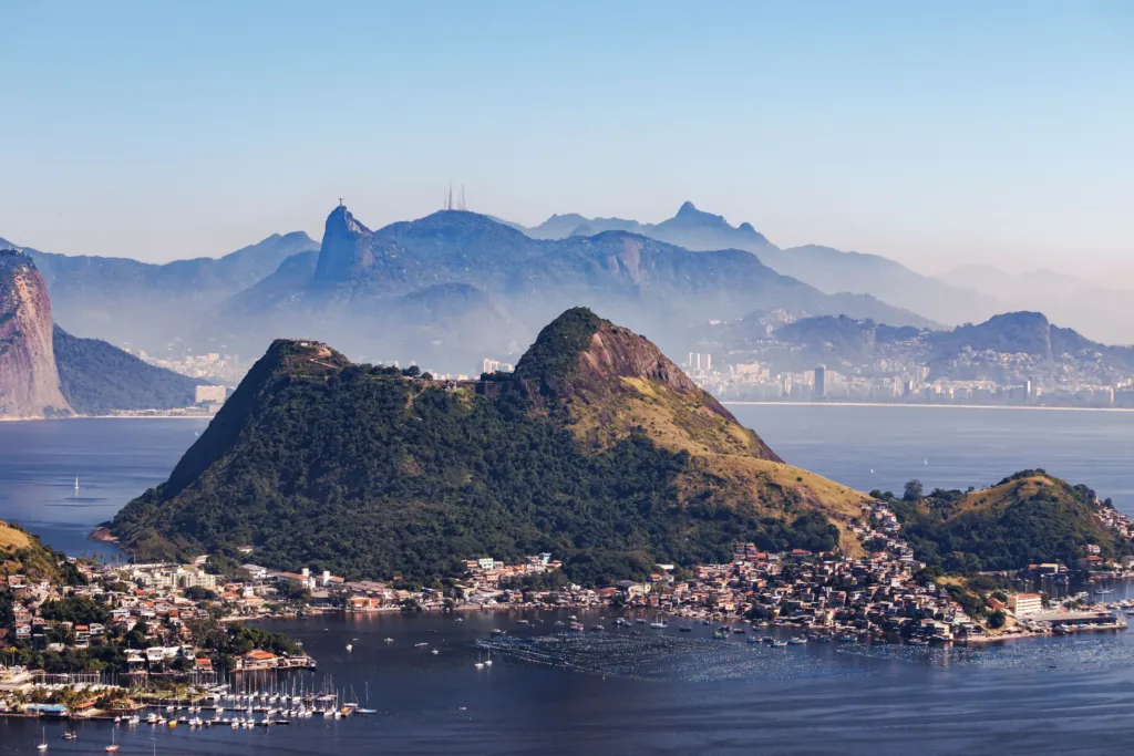 Zalesněné kopce a čtvrť Urca u zátoky Guanabara v Rio de Janeiru, v pozadí horské panorama.