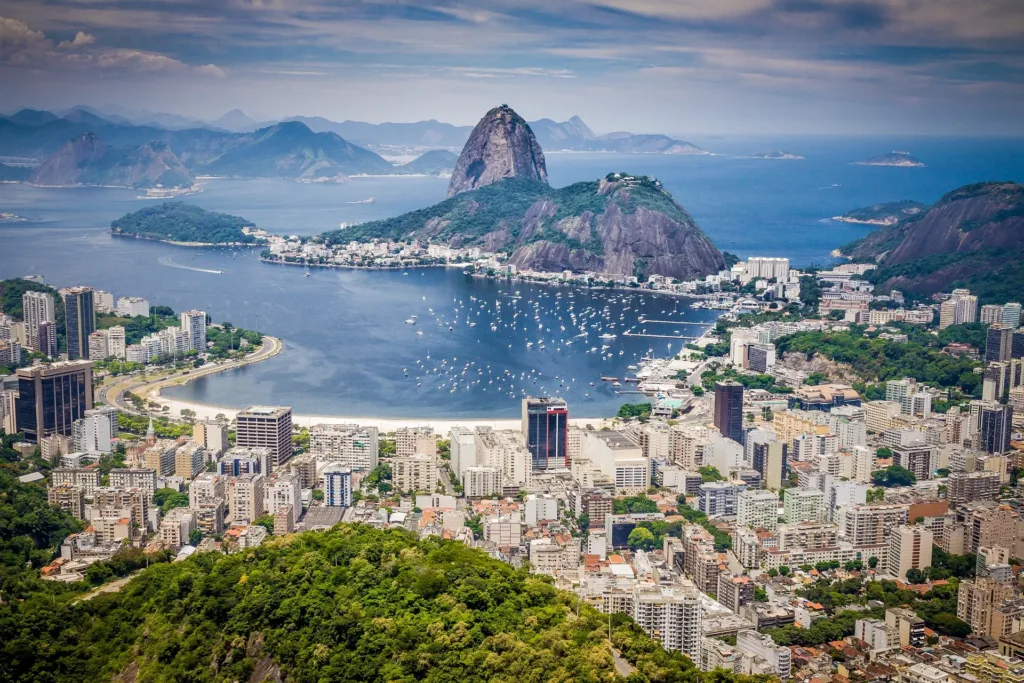 Panoramatický pohled na záliv Guanabara v Rio de Janeiru s horou Cukrová homole, městskou zástavbou a loděmi na hladině.