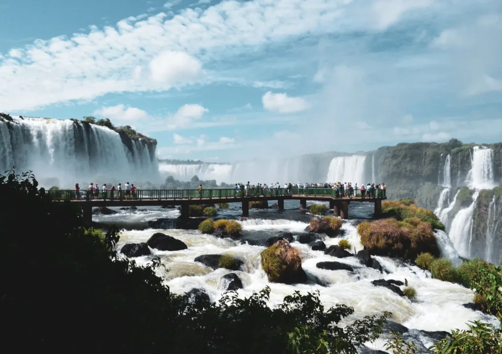 Turisté na vyhlídkové lávce mezi mohutnými vodopády Iguazú v tropické zeleni.