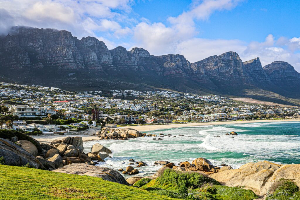 Pobřeží Camps Bay v Kapském Městě s pláží, skalami a pohořím Twelve Apostles v pozadí.