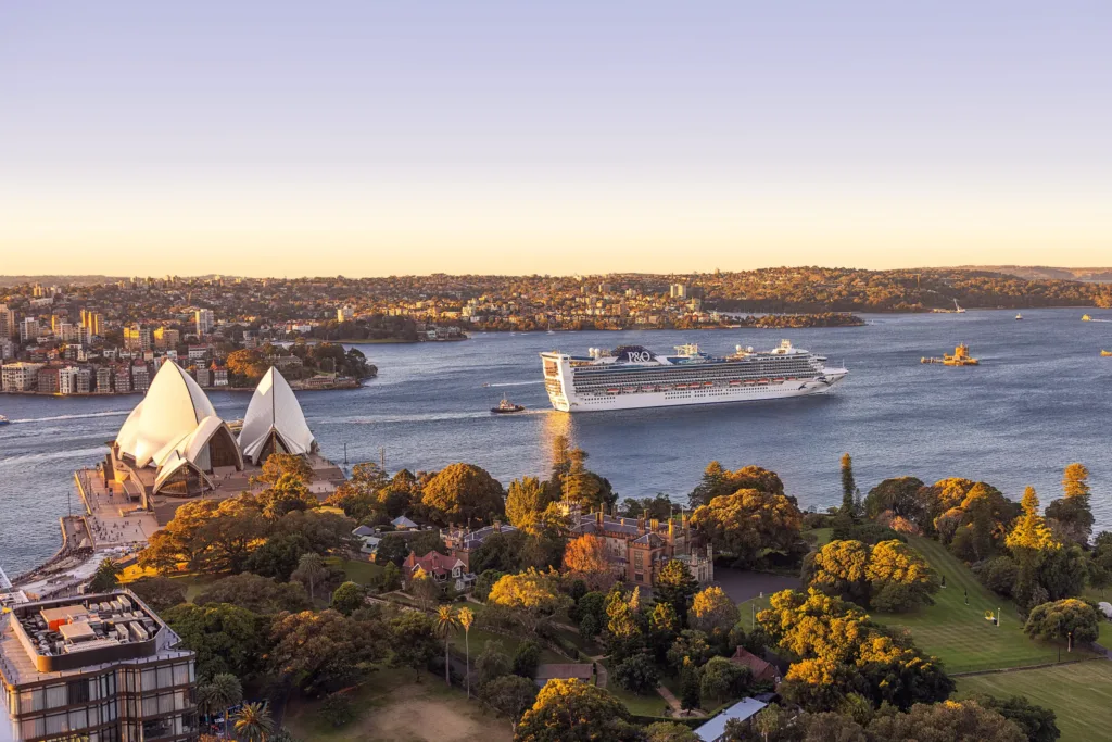 Pohled na sydneyský přístav s bílou budovou opery a projíždějící výletní lodí za soumraku