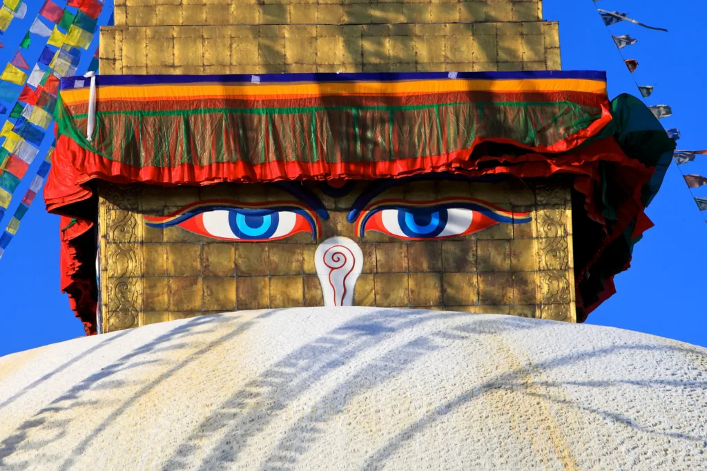 Detail pozlacené stúpy Boudhanath s malovanými Buddhovými očima, barevným baldachýnem a modlitebními praporky.