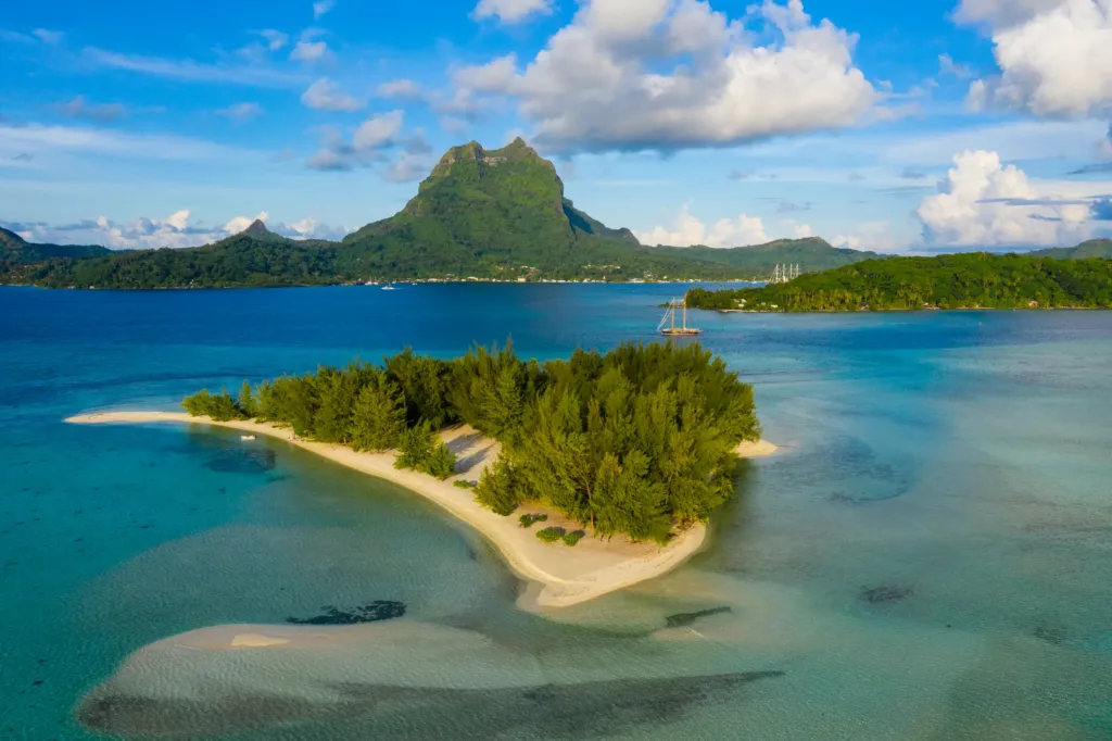 Malý zelený motu v tyrkysové laguně Bora Bora, v pozadí hora Otemanu pod modrou oblohou.