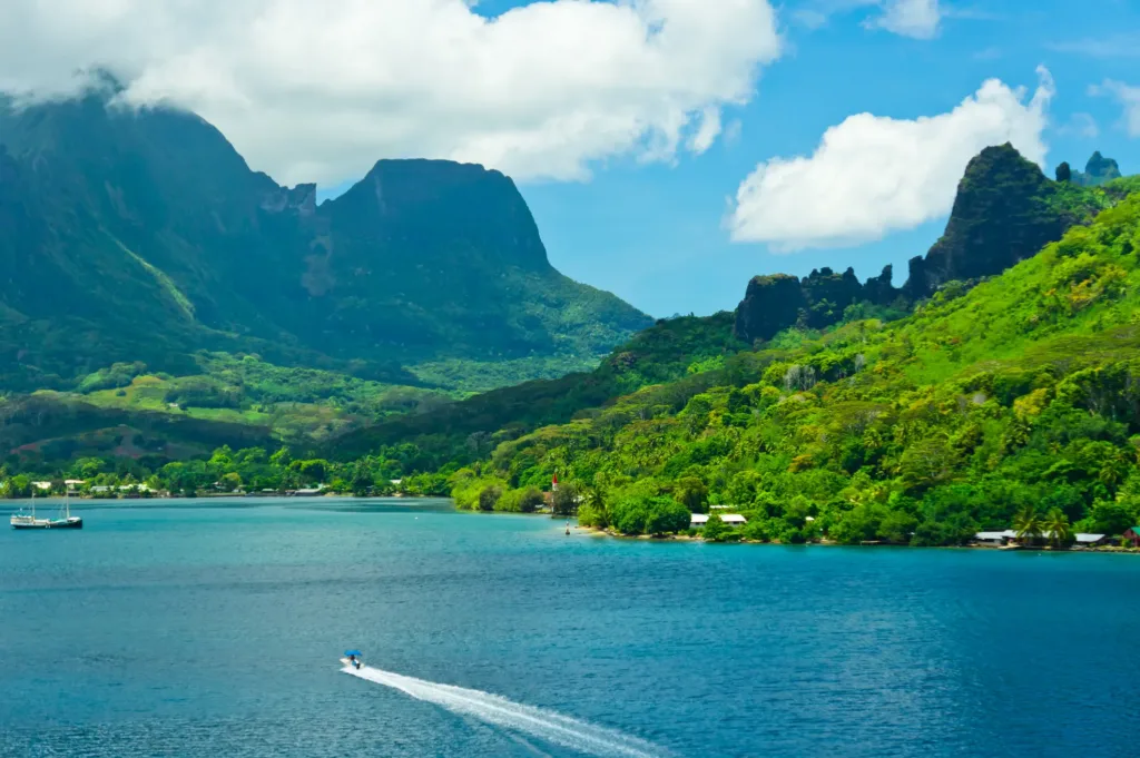 Tyrkysová laguna u zeleného hornatého pobřeží ostrova Moorea s malým člunem na hladině