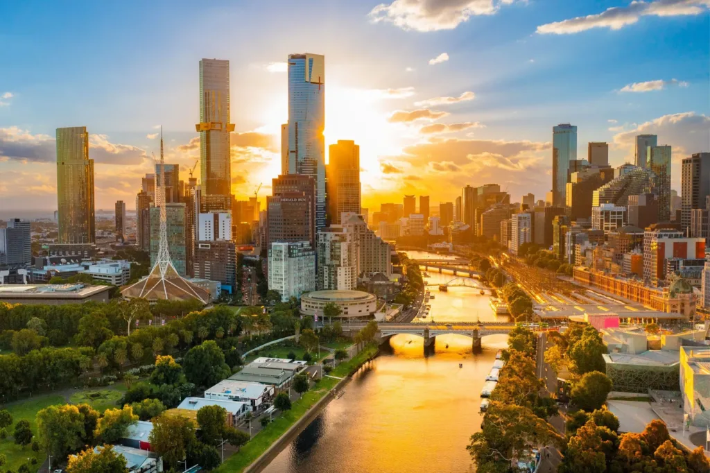 Panorama centra Melbourne s řekou Yarra, mosty, parky a výškovými budovami v teplém světle zapadajícího slunce.