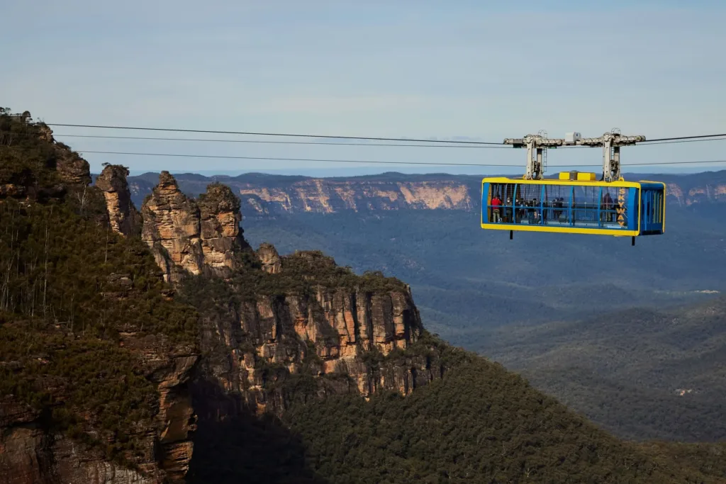Žlutě a modře zbarvená kabina lanovky Scenic Skyway nad zalesněným údolím a skalními útesy v Modrých horách.