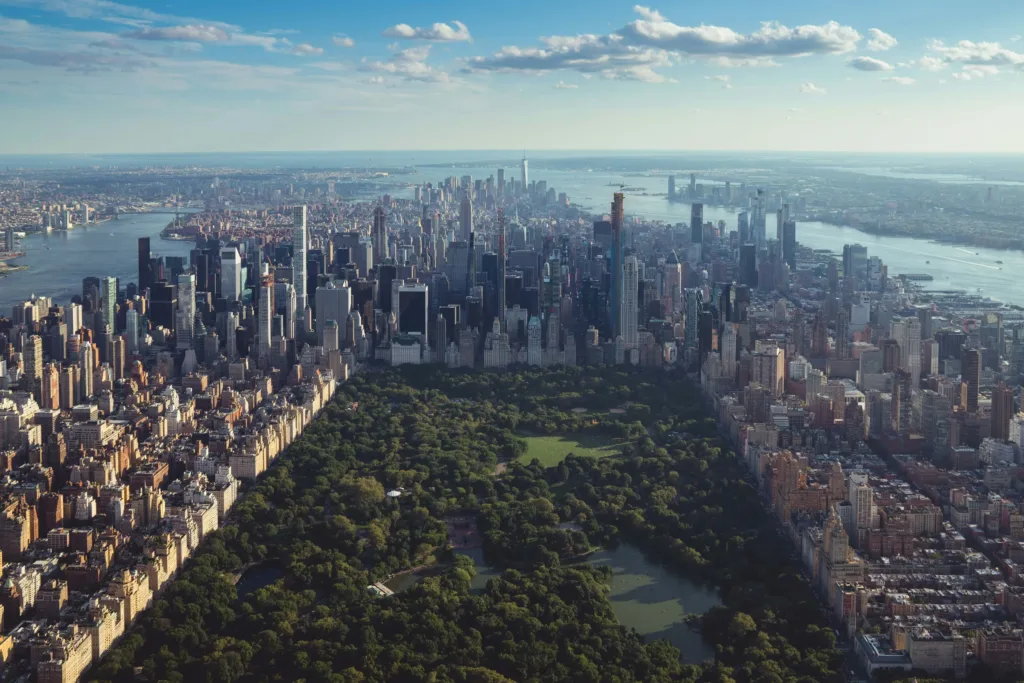 Letecký snímek rozlehlého zeleného parku obklopeného mrakodrapy Manhattanu s řekou a mostem v pozadí