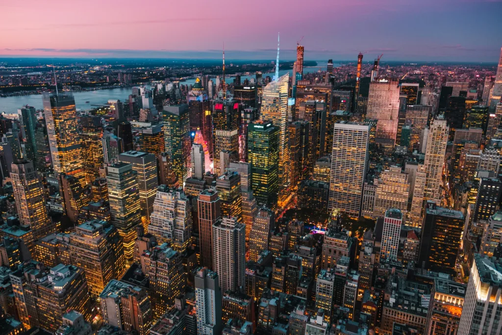 Letecký pohled na mrakodrapy Manhattanu rozsvícené za soumraku s řekou v pozadí